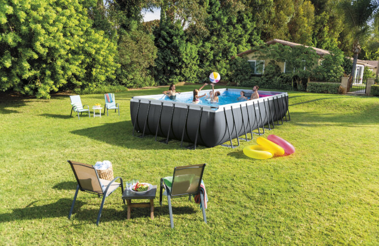 Famille s'amusant dans une piscine hors-sol installée dans un grand jardin, entourée de chaises longues et de jeux d'eau. Exemple d'aménagement extérieur avec piscine hors-sol par Bricomarché Cosne.