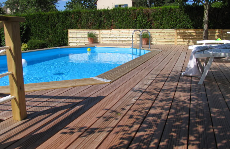 Piscine enterrée entourée d'une terrasse en bois avec des transats, illustrant un aménagement extérieur avec piscine proposé par Bricomarché Cosne.