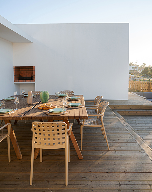 Terrasse aménagée avec un ensemble de mobilier extérieur en bois, comprenant une grande table et des chaises tressées, mise en scène pour un repas en plein air. Vue présentée par Bricomarché Cosne pour l'agencement extérieur.