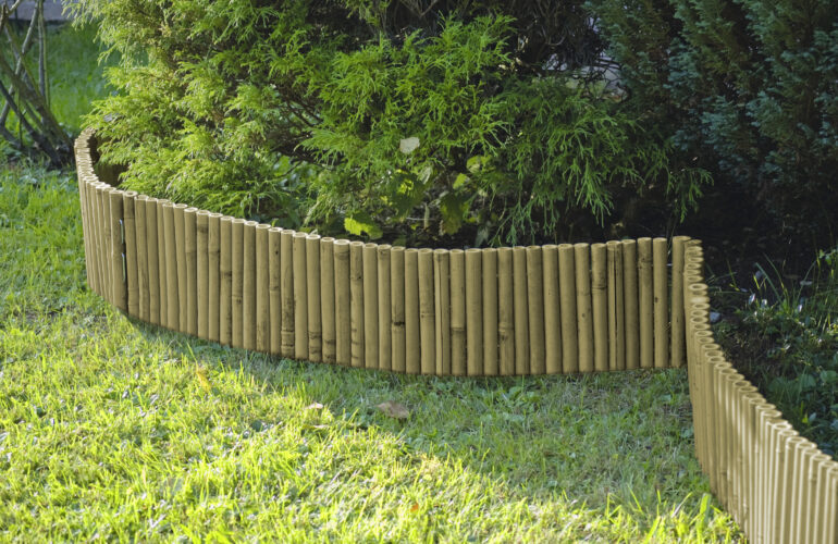 Bordure de jardin en bambou entourant des arbustes verts, délimitant élégamment un espace de verdure. Exemple d'agencement extérieur proposé par Bricomarché Cosne.