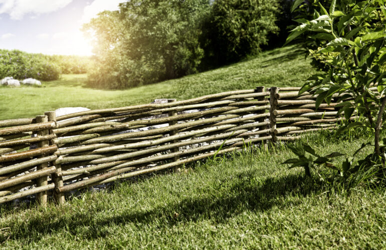 Clôture rustique en bois de noisetier entourant un jardin verdoyant, mettant en valeur un aménagement extérieur naturel et authentique. Exemple d'agencement extérieur par Bricomarché Cosne.