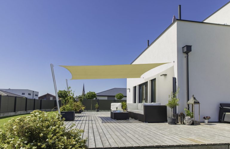 Terrasse en bois moderne équipée de mobilier de jardin confortable et protégée par une voile d'ombrage rectangulaire beige. Exemple d'aménagement extérieur proposé par Bricomarché Cosne.