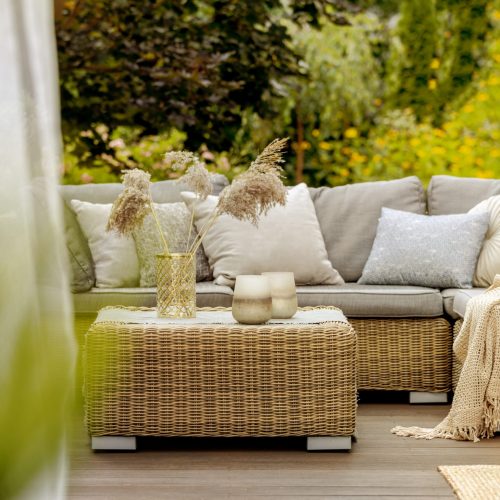 Coin terrasse cosy aménagé avec un canapé en rotin, une table basse assortie et des coussins confortables, entouré de verdure. Exemple d'agencement extérieur proposé par Bricomarché Cosne.